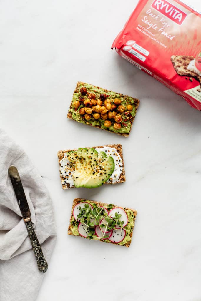 three Ryvita crackers topped with avocado with a package of Ryvita crackers on the side