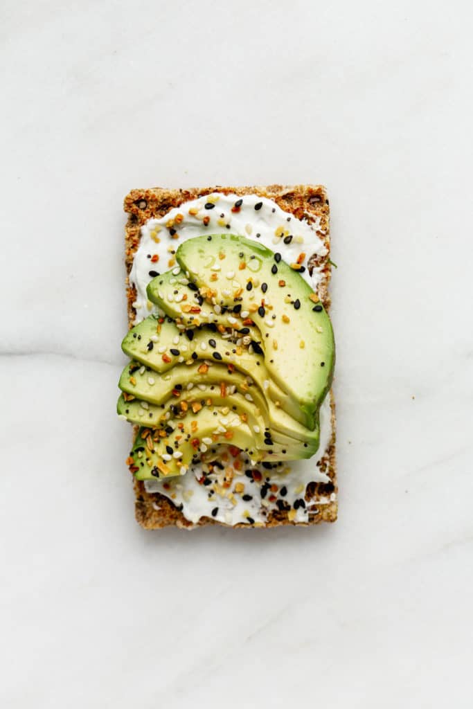A ryvita cracker topped with cream cheese and avocado