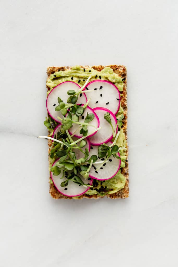 a Ryvita cracker topped with avocado, radishes and radish sprouts