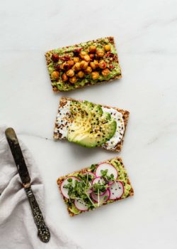 three ryvita crackers topped with avocado with a napkin and knife on the side