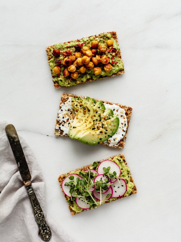 three ryvita crackers topped with avocado with a napkin and knife on the side