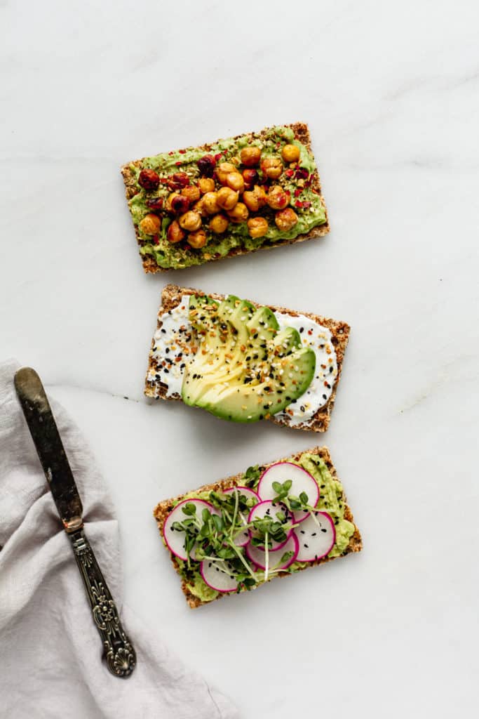 three ryvita crackers topped with avocado with a napkin and knife on the side