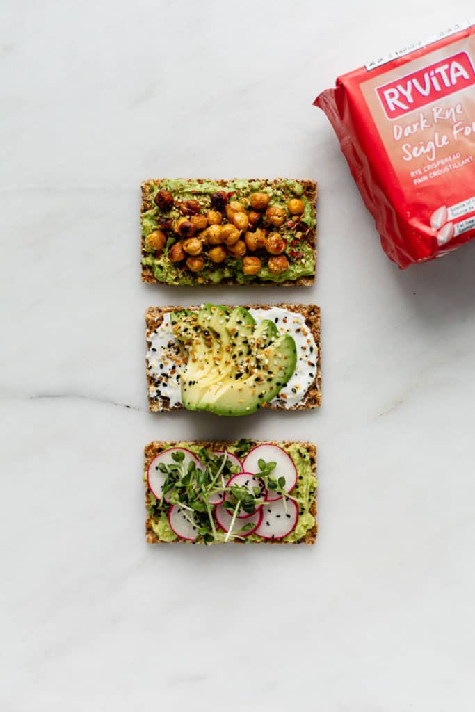 three ryvita crackers topped with avocado with a pack of ryvita on the side