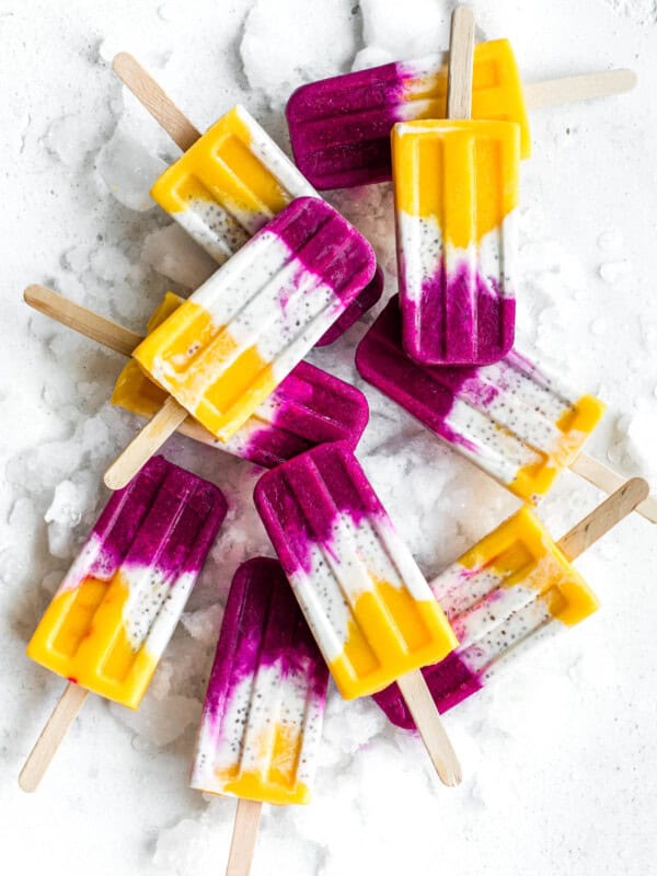 popsicles with layers of mango, coconut and dragonfruit on a board with ice