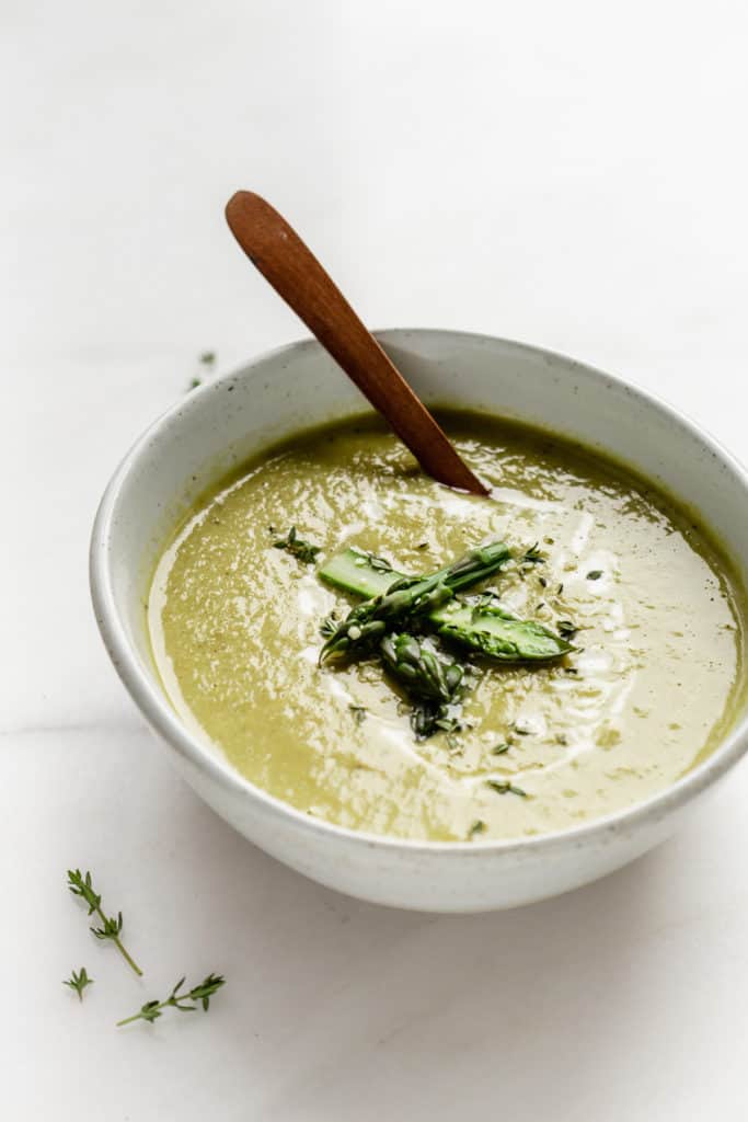 a bowl of asparagus soup with a wooden spoon in it
