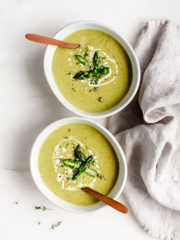 two bowls of vegan asparagus soup with wooden spoons in them and a napkin on the side