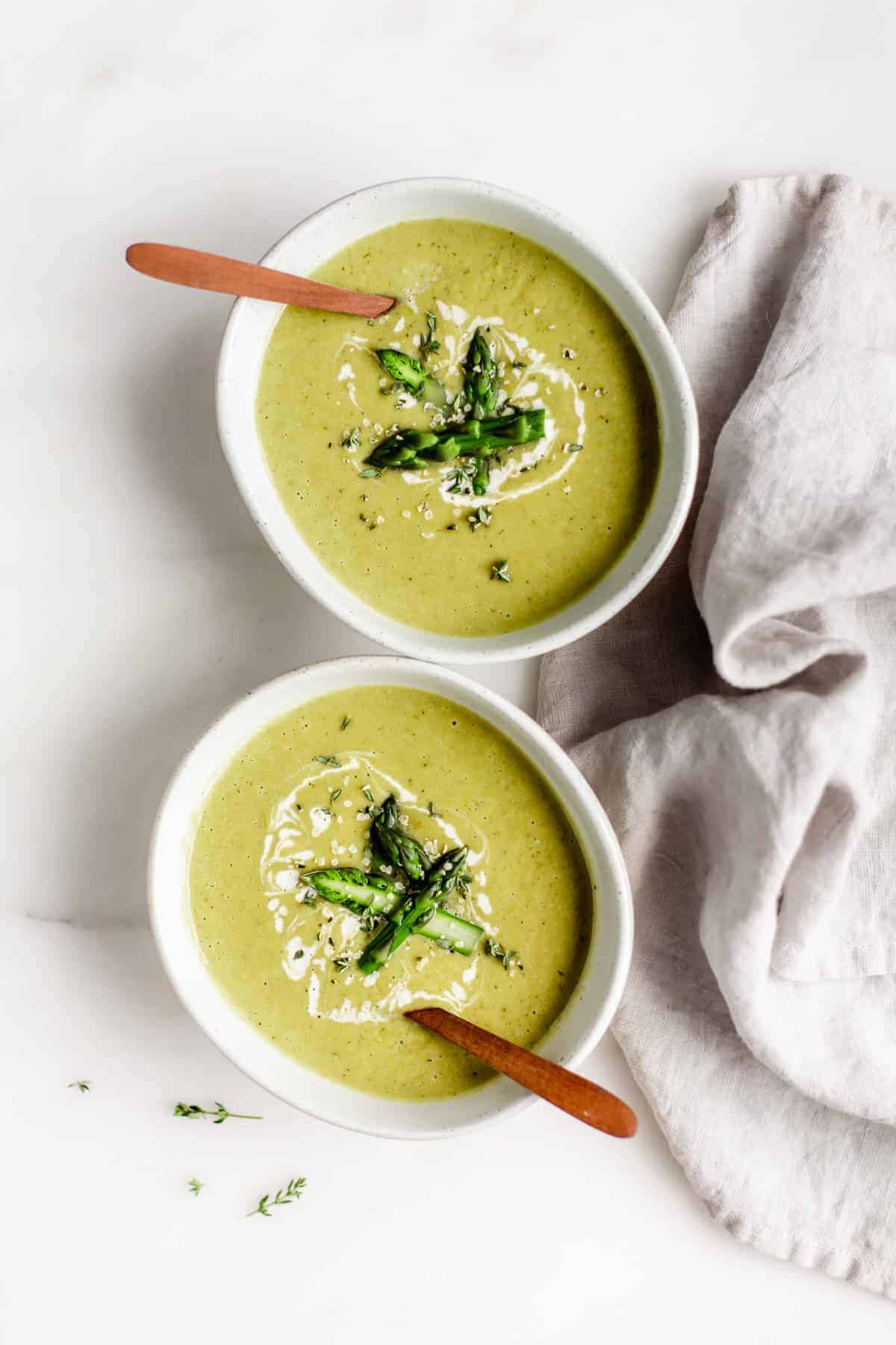 two bowls of vegan asparagus soup with wooden spoons in them and a napkin on the side