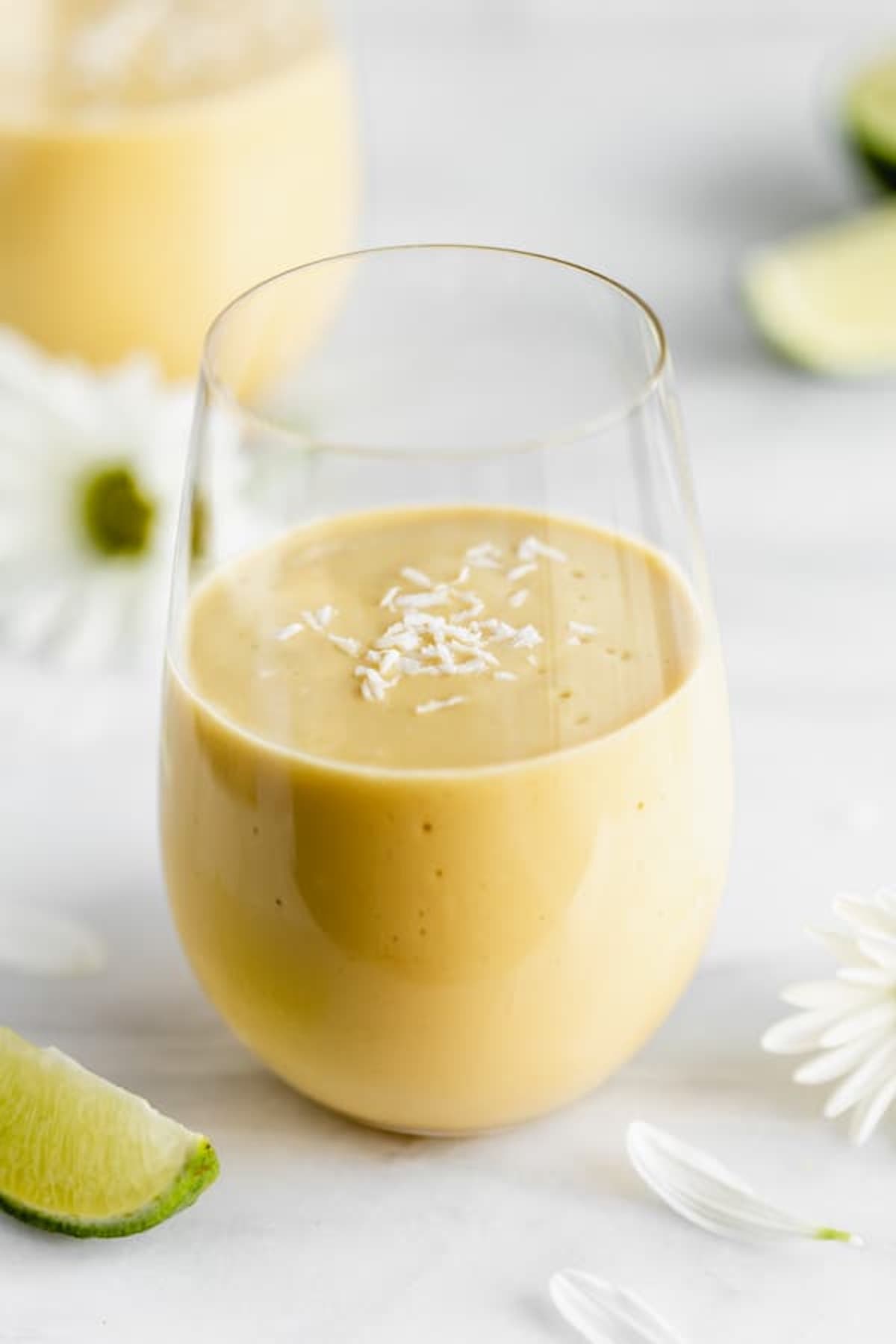 A vegan mango lassi smoothie in a class topped with shredded coconut