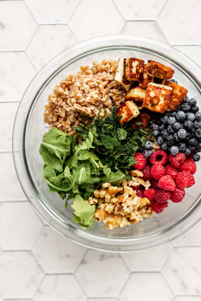 arugula, farro, fried halloumi, blueberries, raspberries and walnuts in a mixing bowl