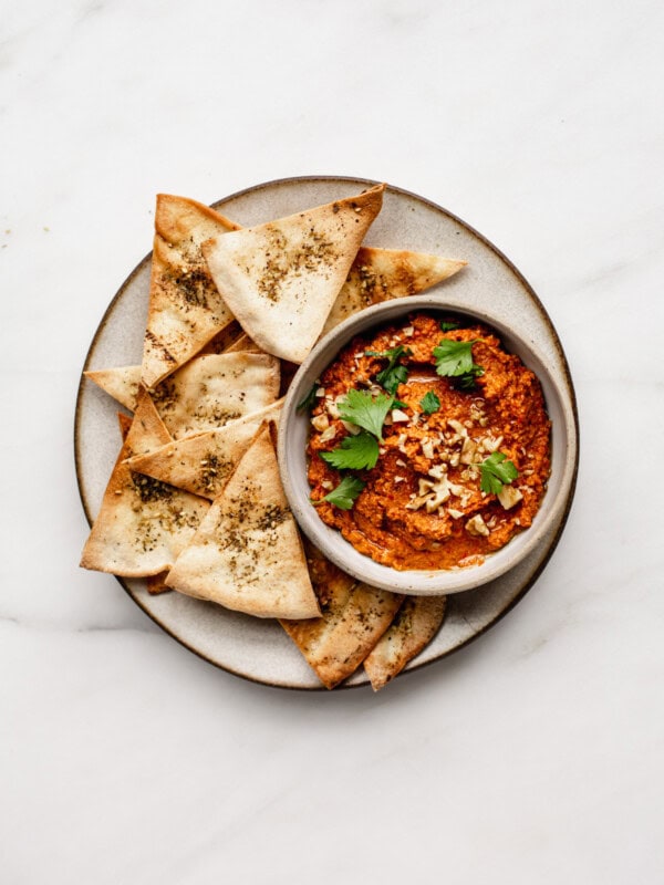 a ceramic plate with pita chips on it and a bowl of roasted red pepper dip