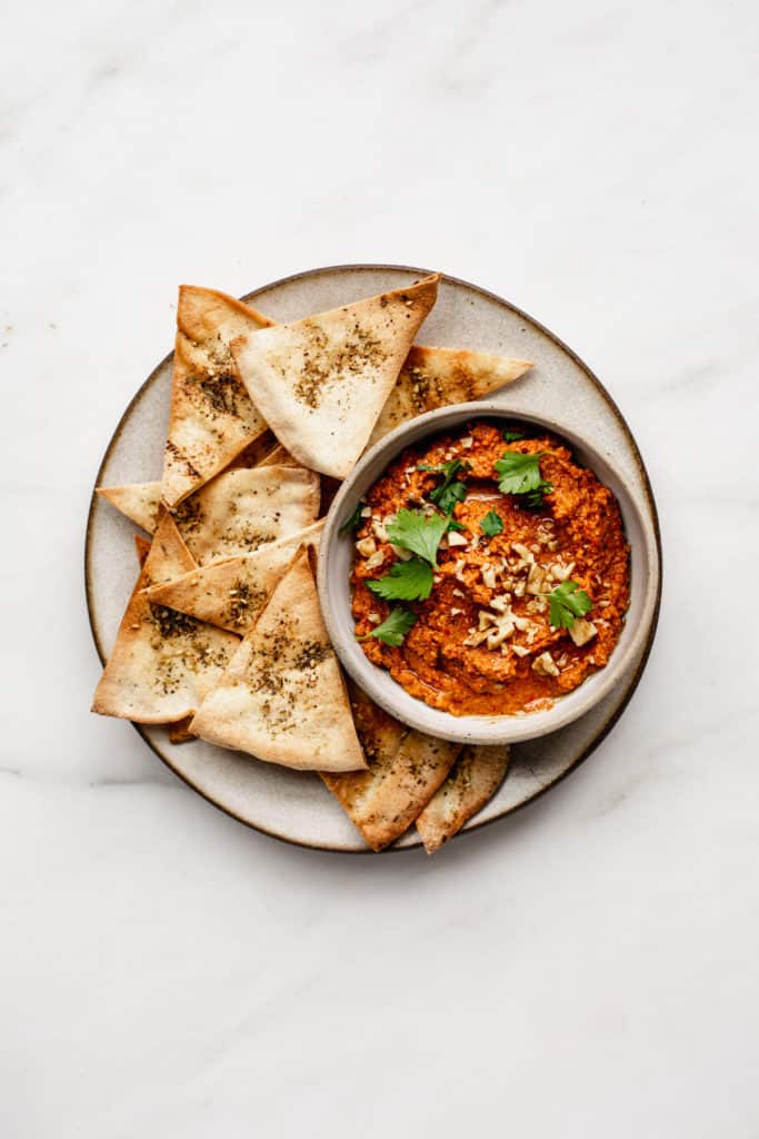 a ceramic plate with pita chips on it and a bowl of roasted red pepper dip