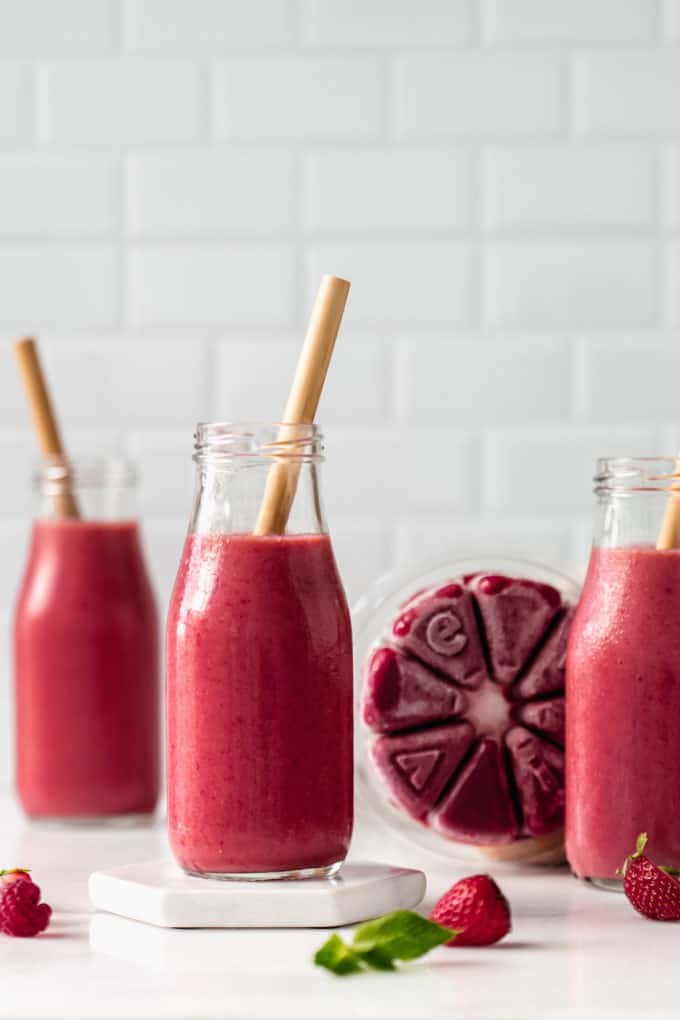 A red smoothie in a small bottle with a wheel of smoothie cubes