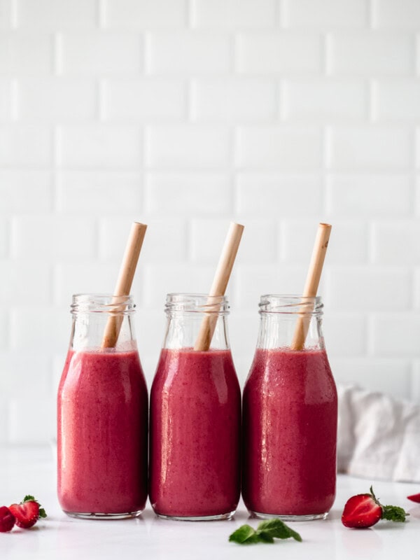 three bottles of berry smoothie with bamboo straws in them