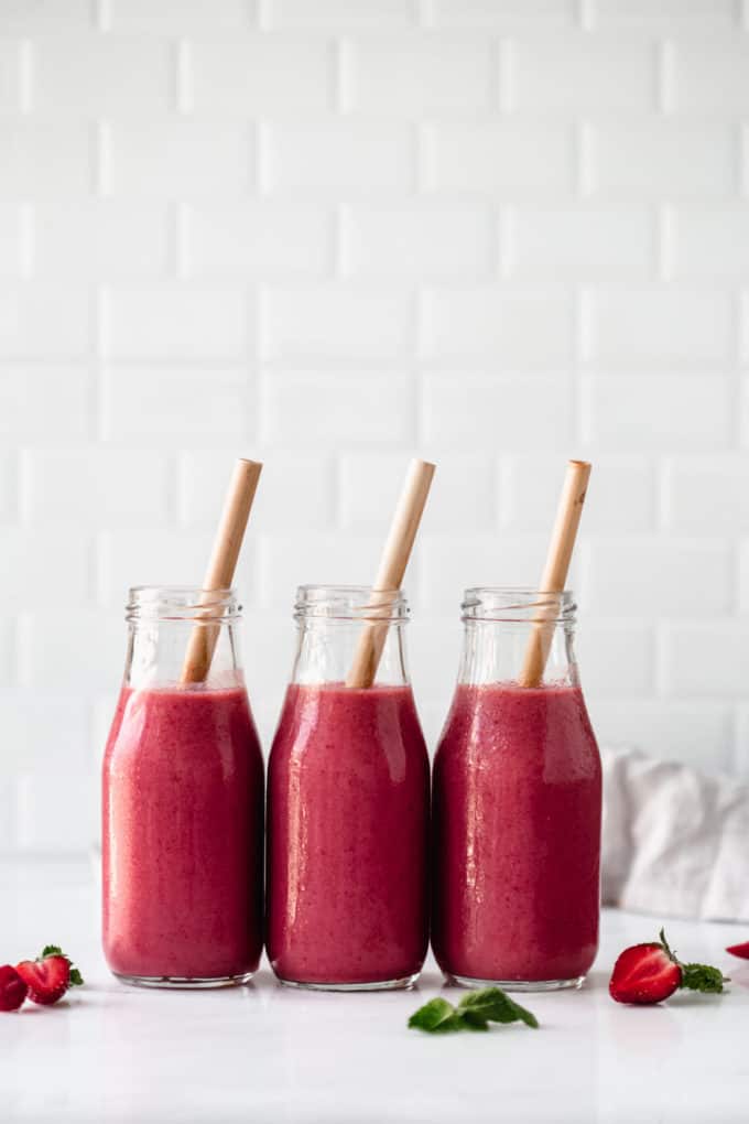 three bottles of berry smoothie with bamboo straws in them
