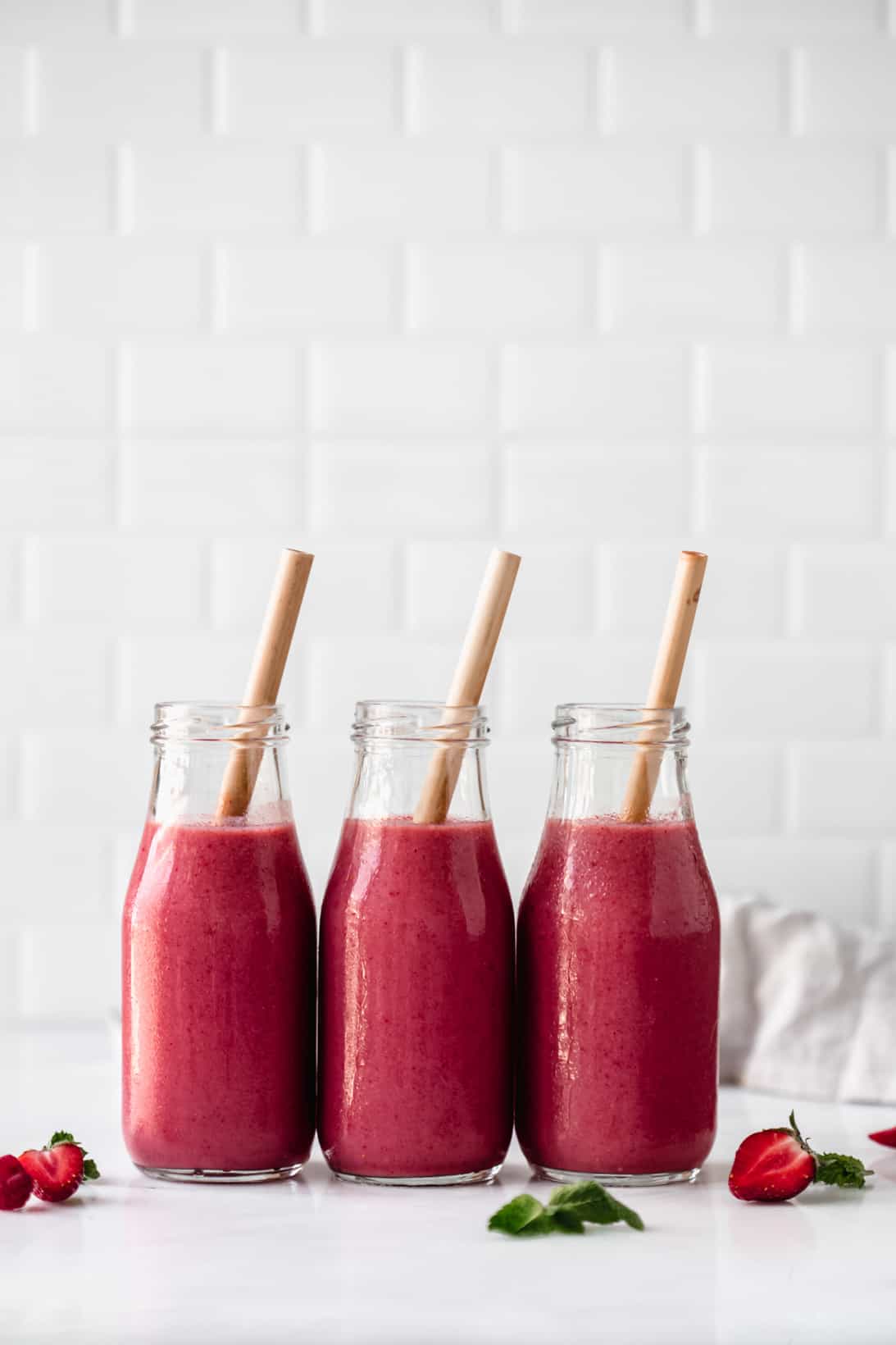 three bottles of berry smoothie with bamboo straws in them