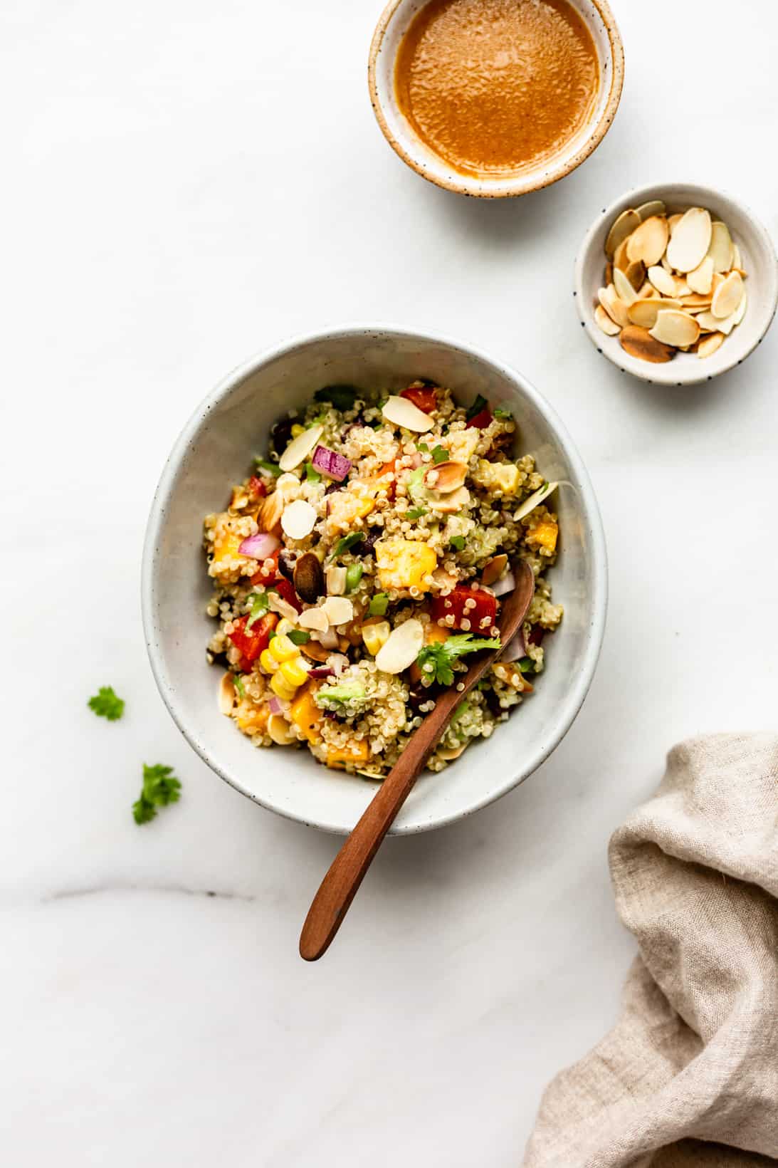A bowl of southwest quinoa salad with two small bowls of salad dressing and toasted almonds on the side