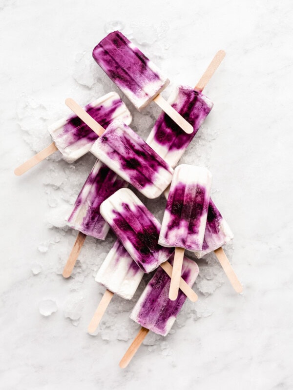 blueberry greek yogurt popsicles stacked on ice on a marble board