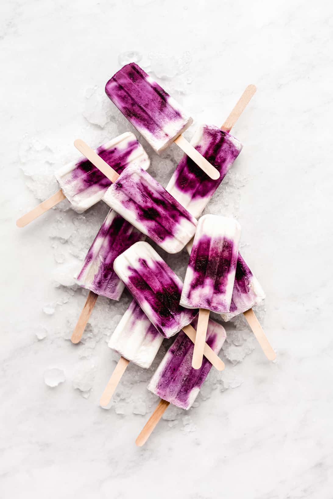 blueberry greek yogurt popsicles stacked on ice on a marble board