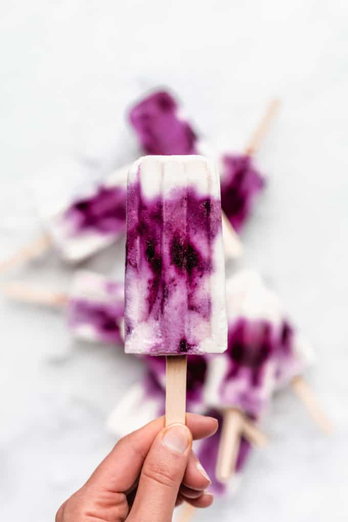 a hand holding a blueberry greek yogurt popsicle