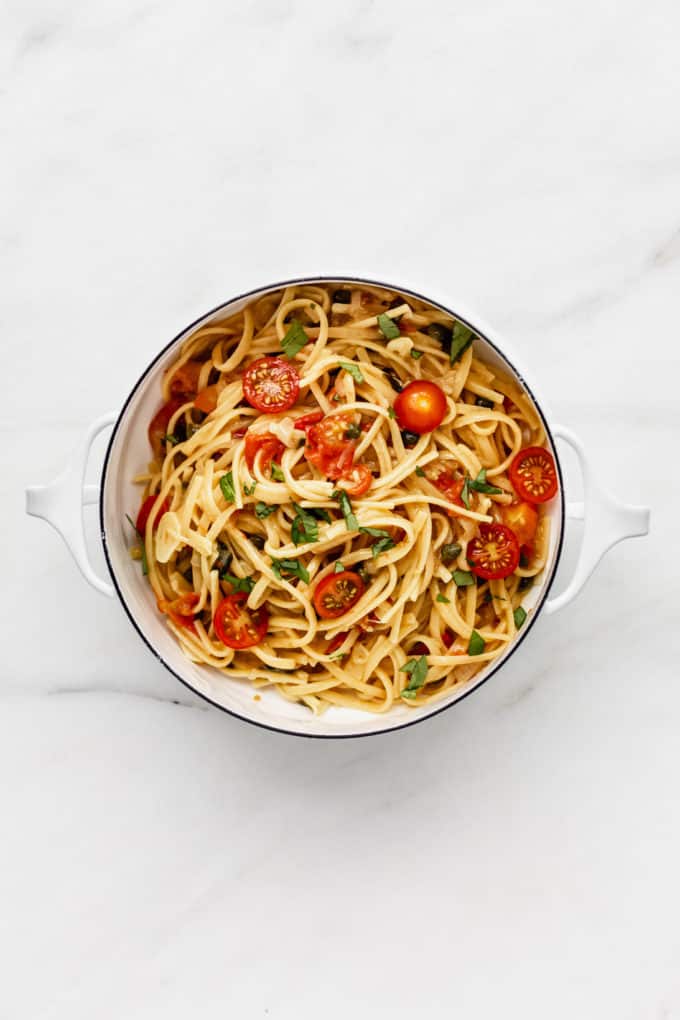 a white pot filled with linguine pasta, cherry tomatoes, capers and basil