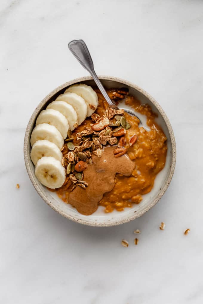 pumpkin pie oatmeal in a bowl topped with bananas, granola and almond butter
