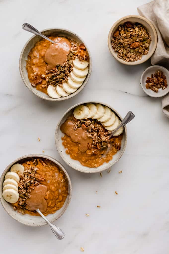 three bowls of pumpkin pie oatmeal with small bowls of granola and pecans on the side