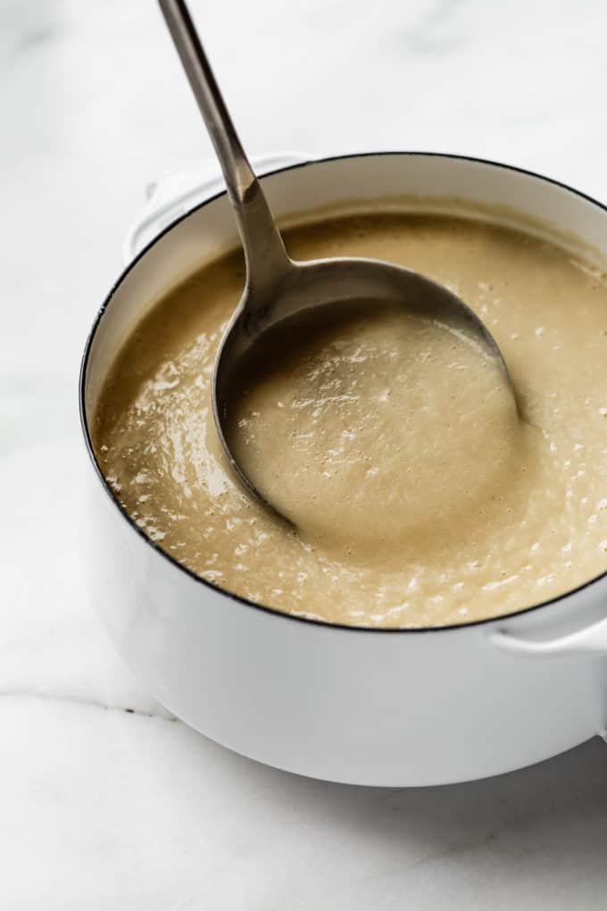 a ladle scooping garlic soup out of a white pot