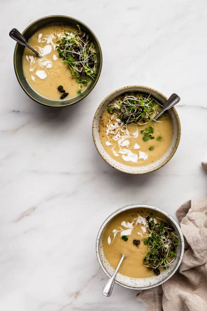 three bowls of roasted garlic soup on a marble board with a beige napkin on the side