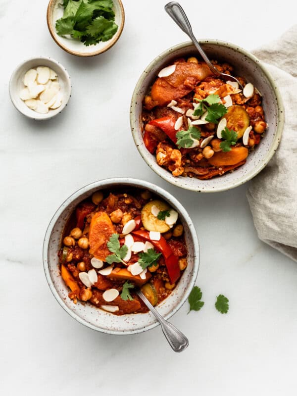 two bowls of vegetable tagine with two small bowls of almonds and cilantro on the side