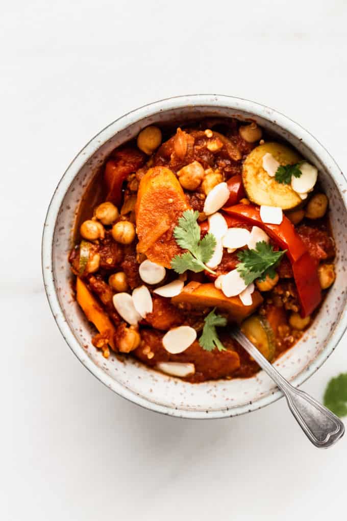 A bowl filled with vegetable tagine topped with almonds and cilantro
