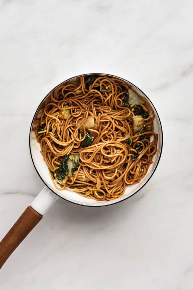 teriyaki noodles with bok choy in a white pot with a wood handle