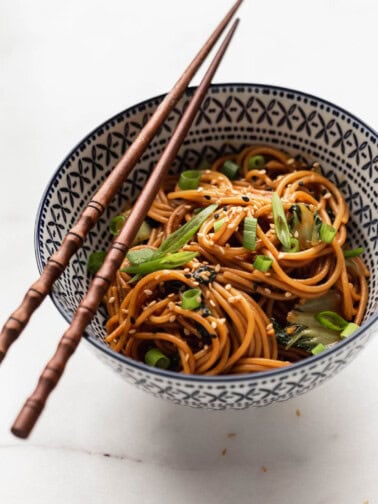 a bowl of noodles topped with green onions and sesame seeds