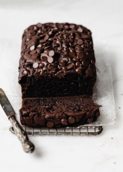 A loaf of healthy chocolate pumpkin bread topped with chocolate chips with a small knife on the side