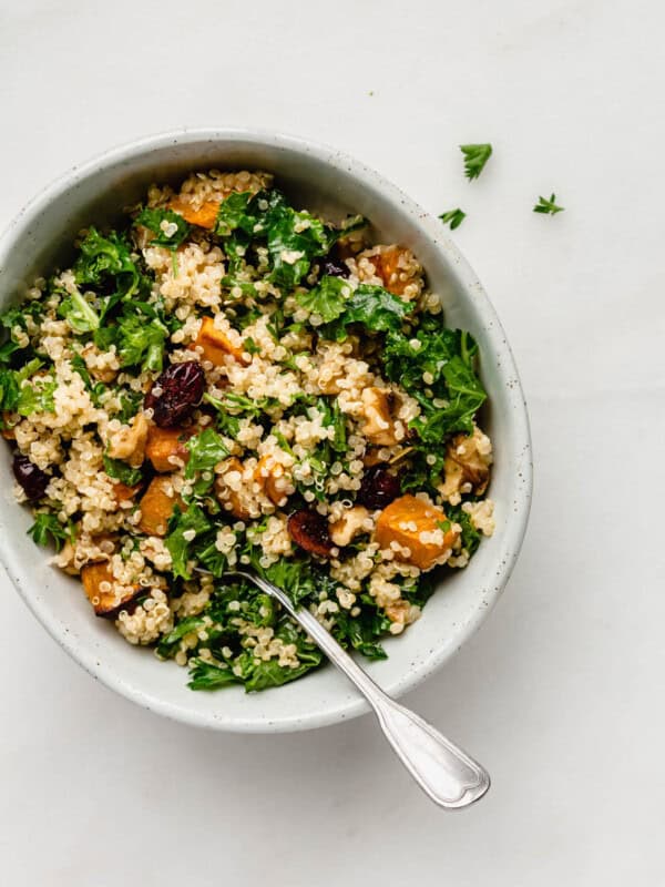 Quinoa and kale salad with sweet potatoes and cranberries in a bowl with a spoon