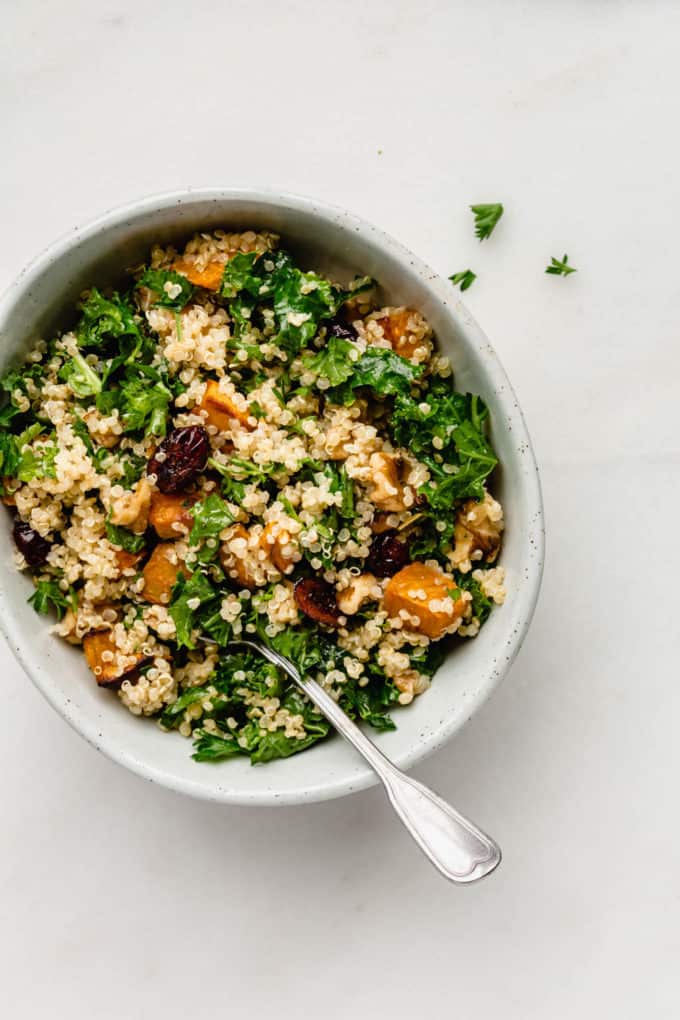 Quinoa and kale salad with sweet potatoes and cranberries in a bowl with a spoon