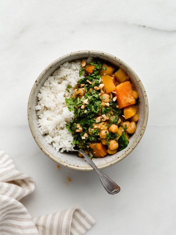 A bowl filled with white rice and pumpkin chickpea curry topped with cilantro and peanuts