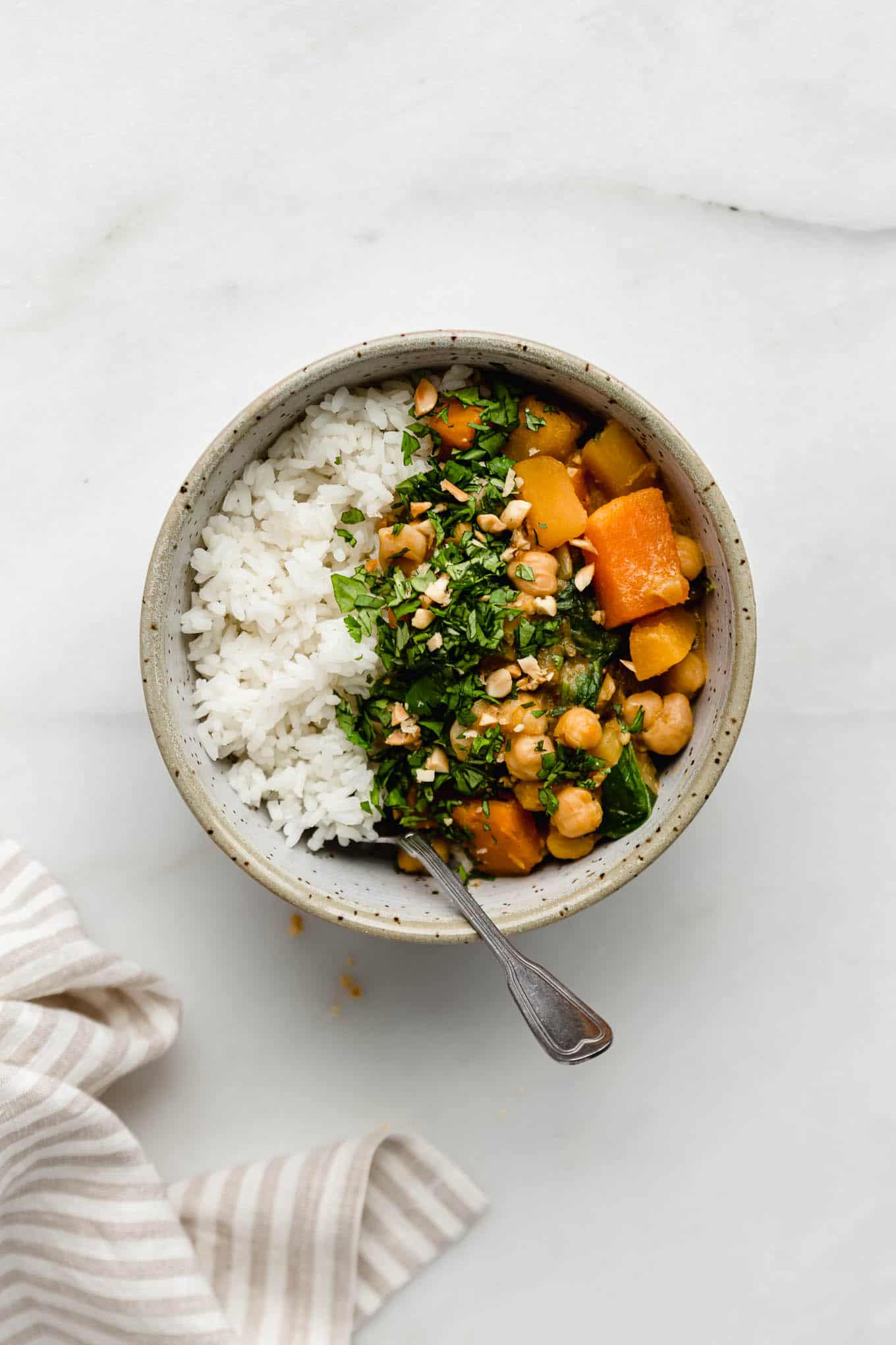 A bowl filled with white rice and pumpkin chickpea curry topped with cilantro and peanuts