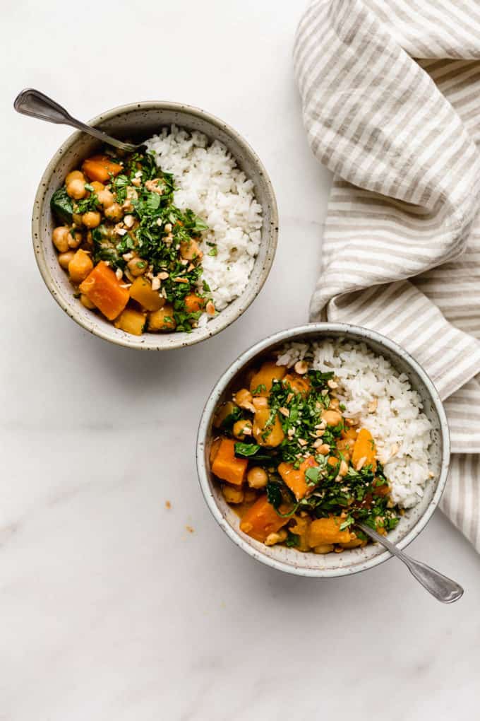 Two bowls of pumpkin curry and rice with a striped beige napkin on the side
