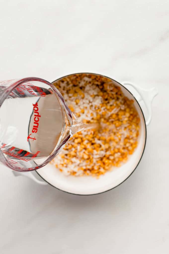 a measuring cup pouring water into a pot of peas and rice
