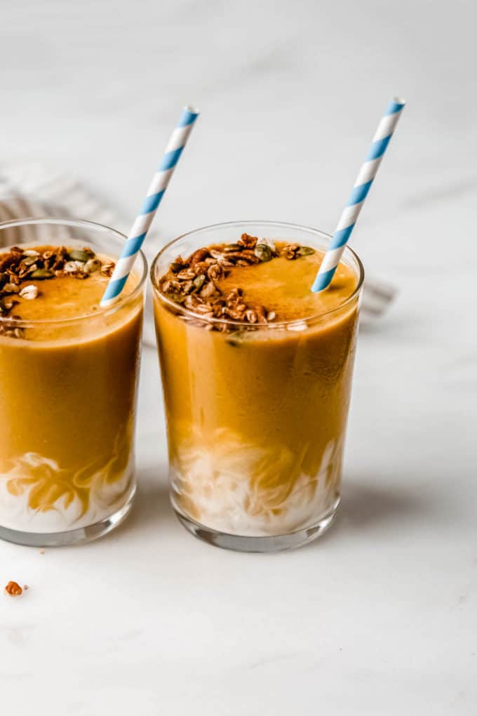 Two pumpkin smoothies next to each other with a striped blue straw in them