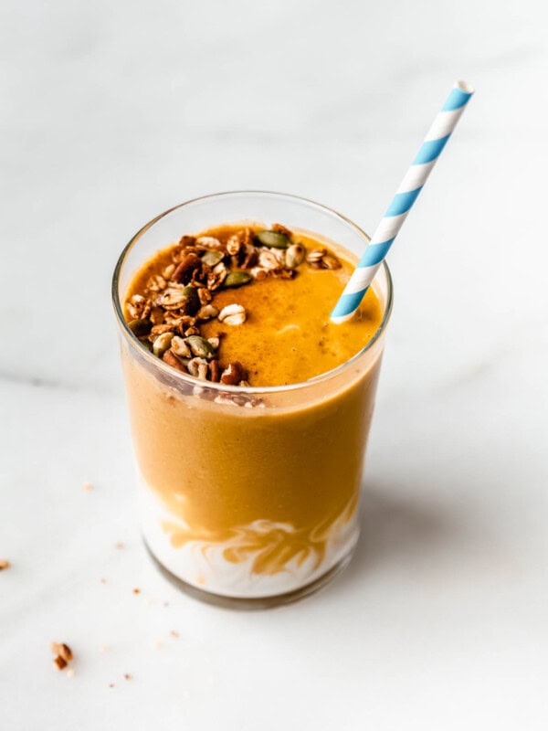 a pumpkin pie smoothie topped with granola with a striped blue and white straw in it