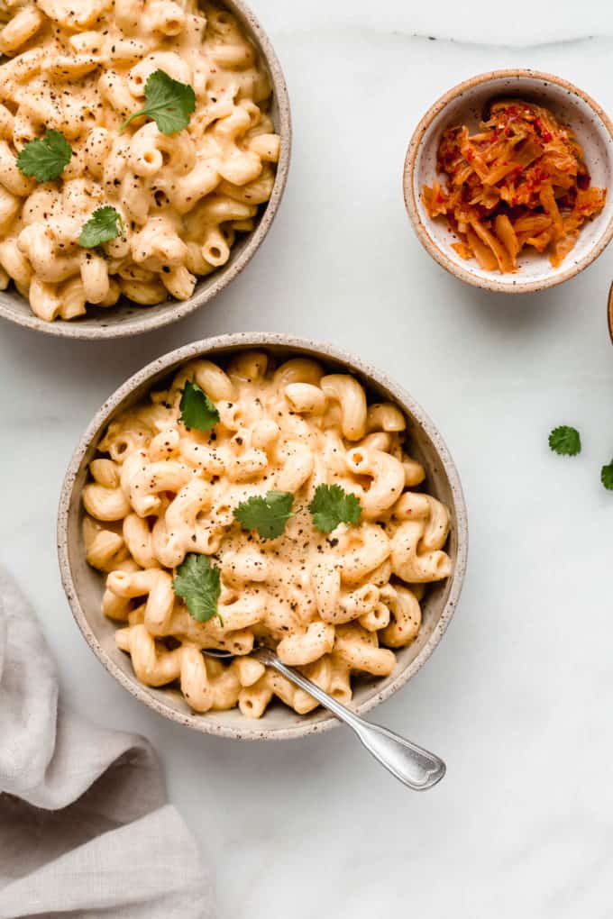 Two bowls of vegan kimchi mac and cheese with some kimchi on the side in a small bowl