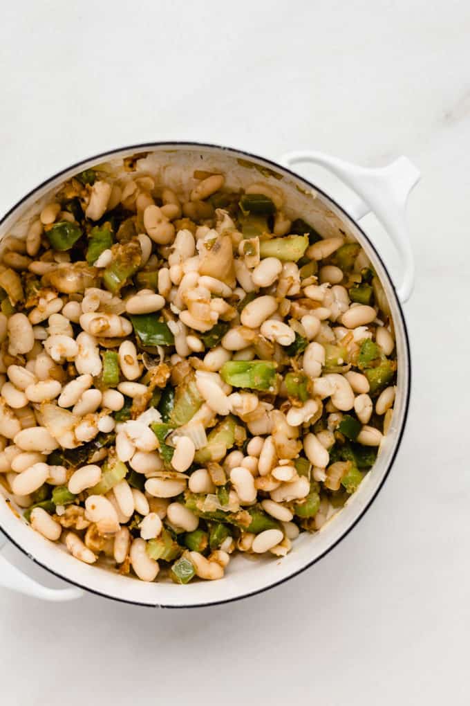 A white pot with white beans and peppers in it
