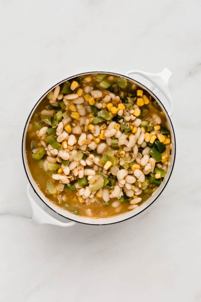 A white pot with broth, white beans, green peppers and corn in it