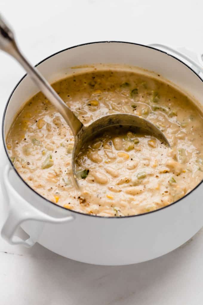 A white pot with a ladle scooping white chili