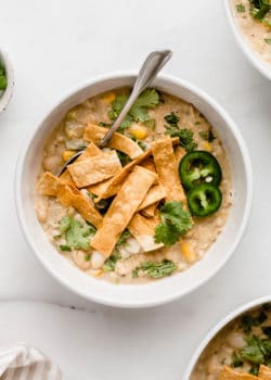 A white bowl with white vegan chili in it topped with tortilla strips and cilantro
