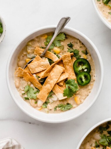 A white bowl with white vegan chili in it topped with tortilla strips and cilantro