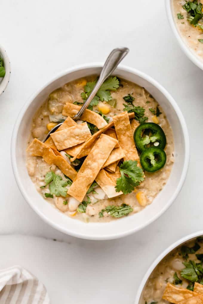 A white bowl with white vegan chili in it topped with tortilla strips and cilantro