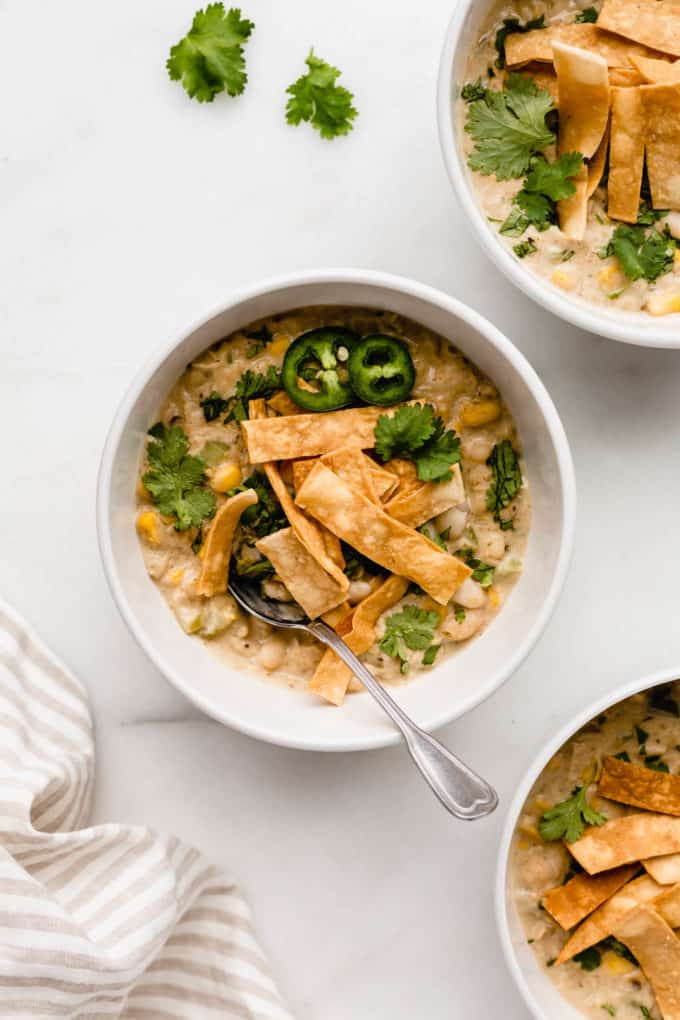 A bowl of white bean chili topped with tortilla chips with a napkin on the side