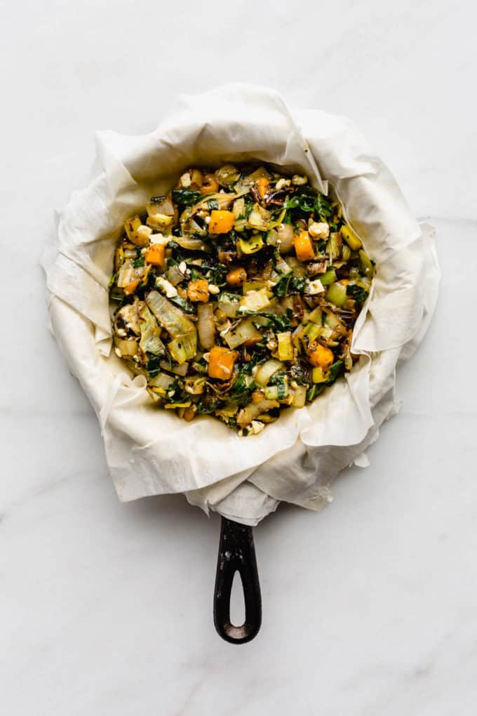 phyllo dough draped over a cast iron skillet filled with sauteed veggies